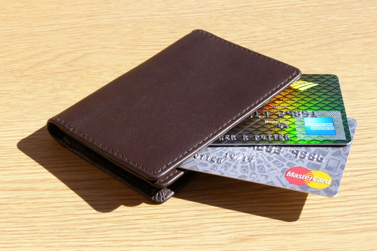 A brown wallet with two credit cards sticking out lays on a wooden table