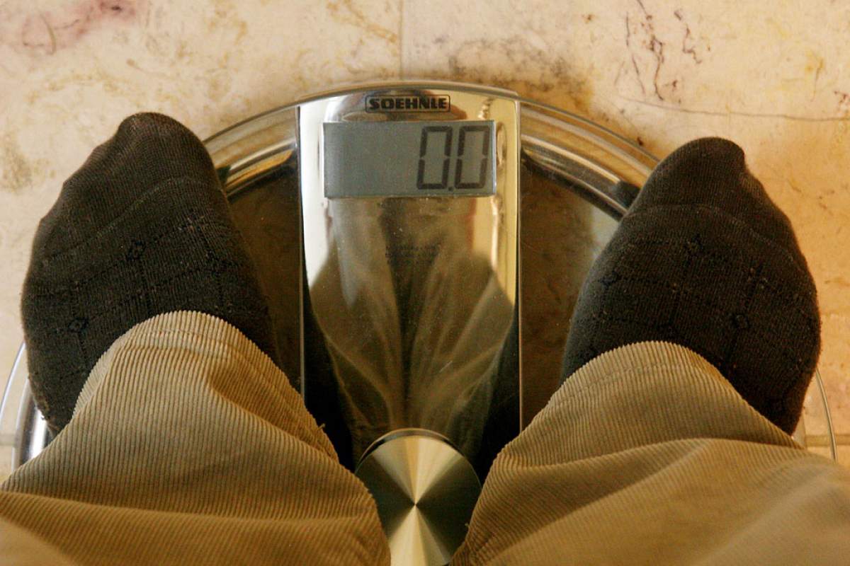 man standing on a weight-measuring scale in black socks and khakis