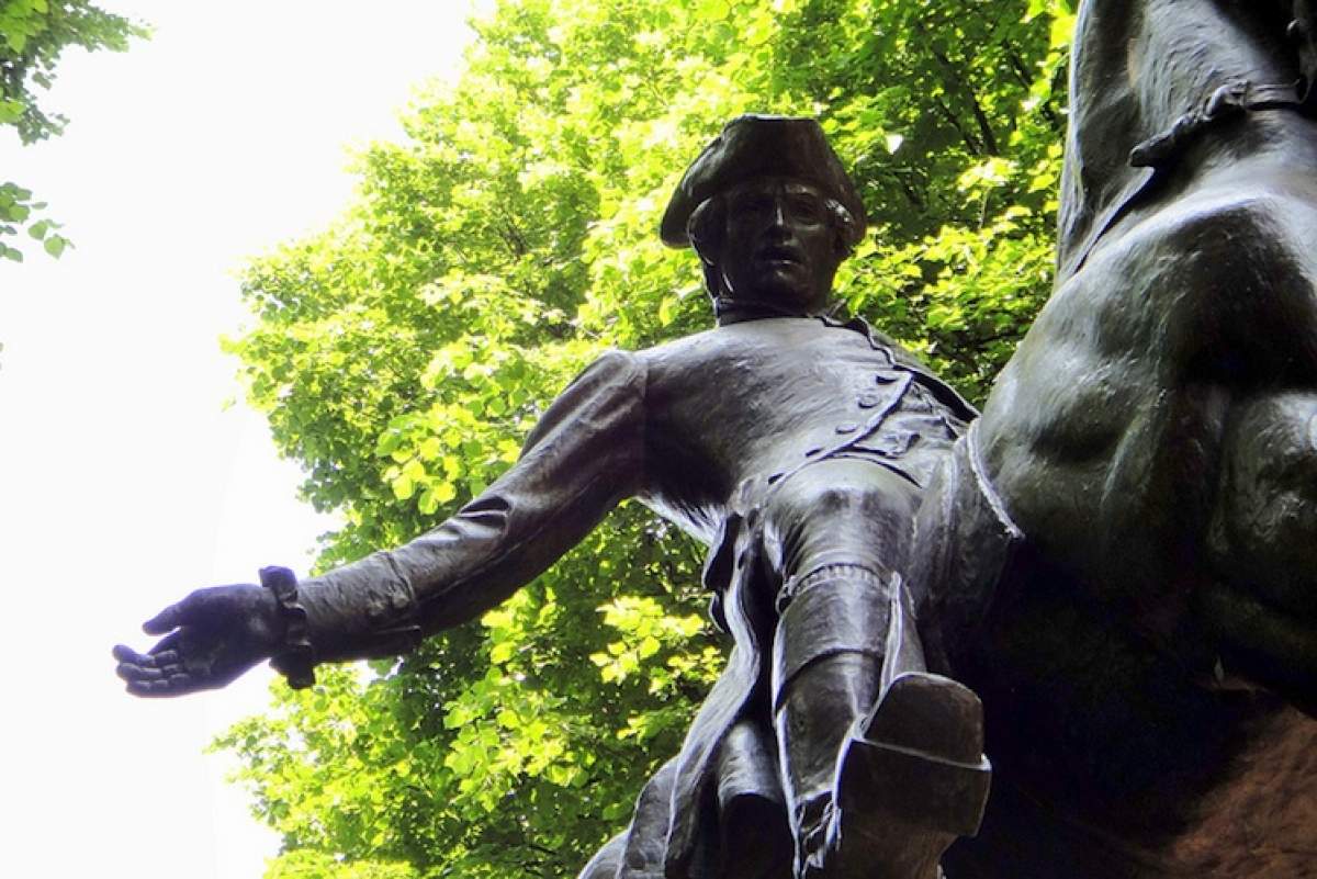 A statue of Paul Revere under a canopy of green trees