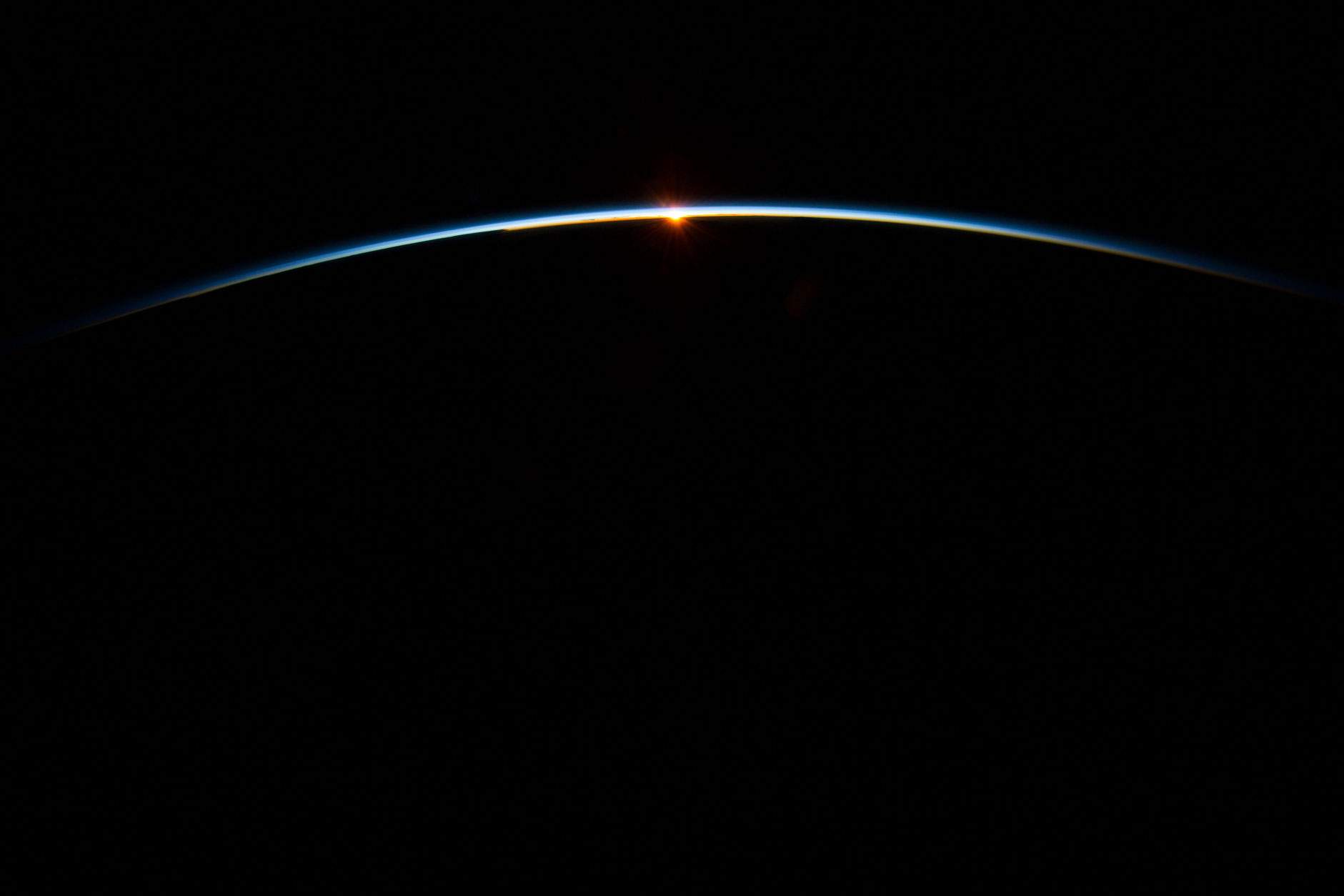 The sun, peeking through the thin line of Earth's atmosphere, photographed from the International Space Station.