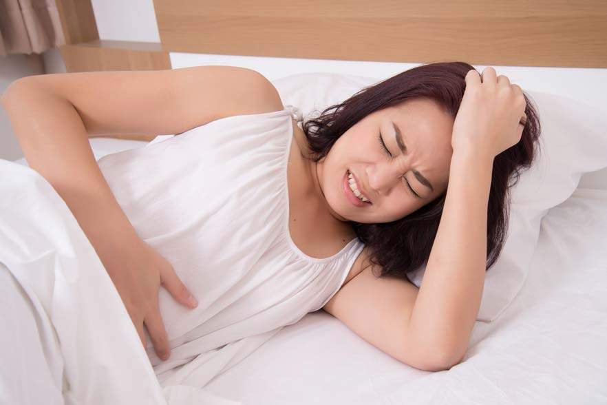 woman in bed holds stomach in pain