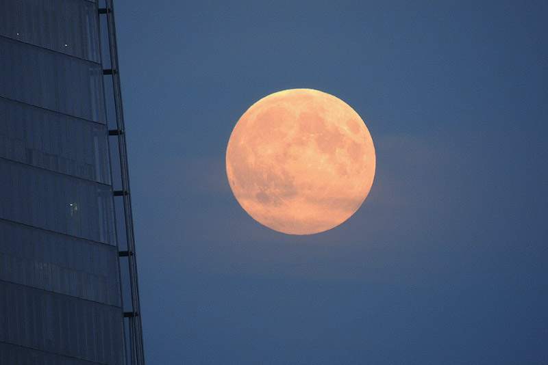 A full moon that appears large and orange hovers in the London sky
