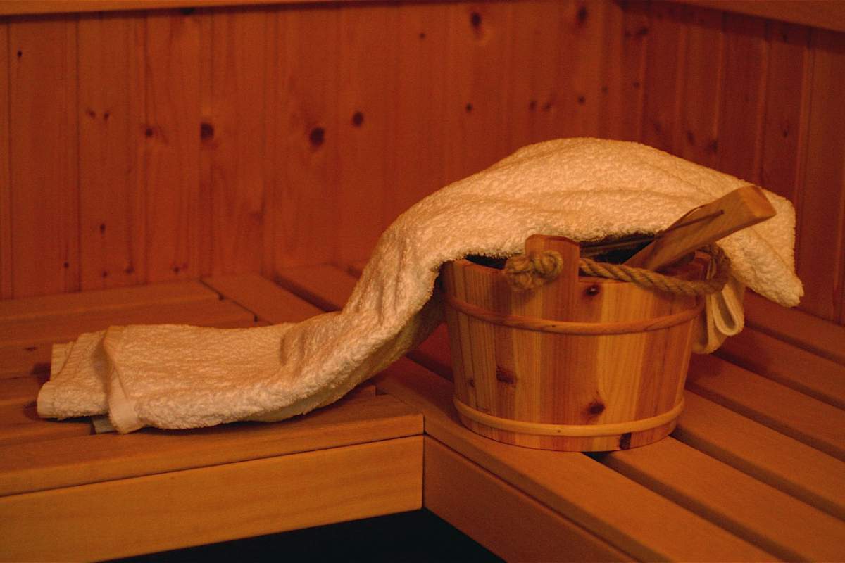 A corner of a sauna: brown wood bench, brown wood walls. A basket with a white towel spread over it.