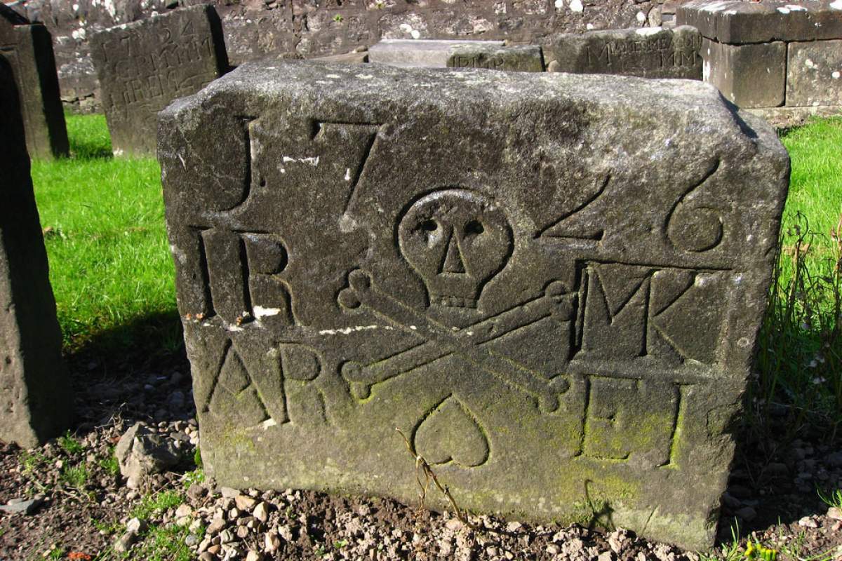 A very old gravestone with a detail of a skull and crossbones. More gravestones behind it.