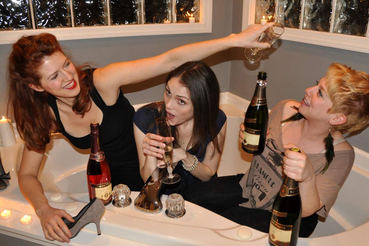 three girls in a bath tub with champagne