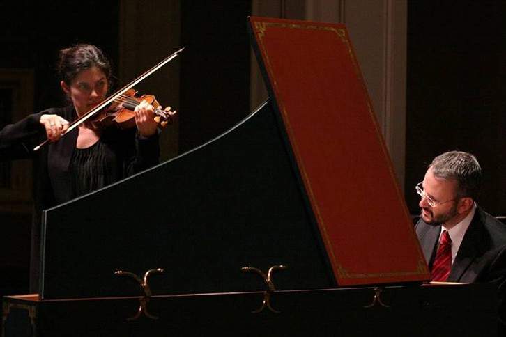a woman stand playing the violin and a man plays the harpsichord.