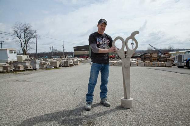 limestone carver stands with his sculpture of an enormous pair of stone scissors