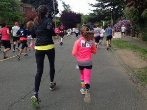 A woman and a young girl running in a marathon, backs turned towards the camera