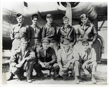 The crew of nine is posed in front of a plane.