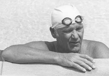 Doc, in swim cap and goggles, leans over the side of the pool.