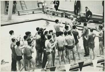 The team gathers around Doc at poolside. He holds up the trophy while they cheer.