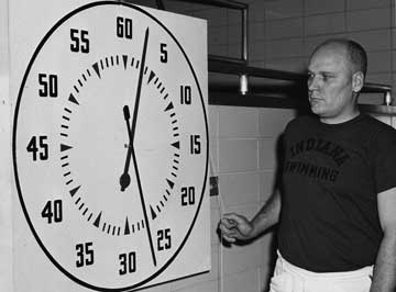 Doc stands to the right of a large pace clock in the pool area.