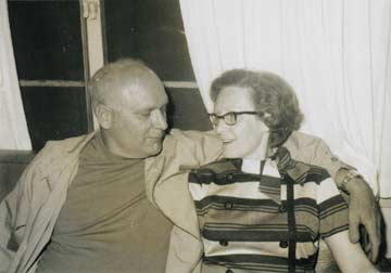 Doc and Marj sit together on a couch, looking happily at each other.