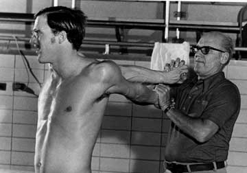 Doc stands behind swimmer Jim Montgomery, stretching his arms.