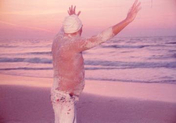 Doc stands, arms outstretched, on a sandy beach.