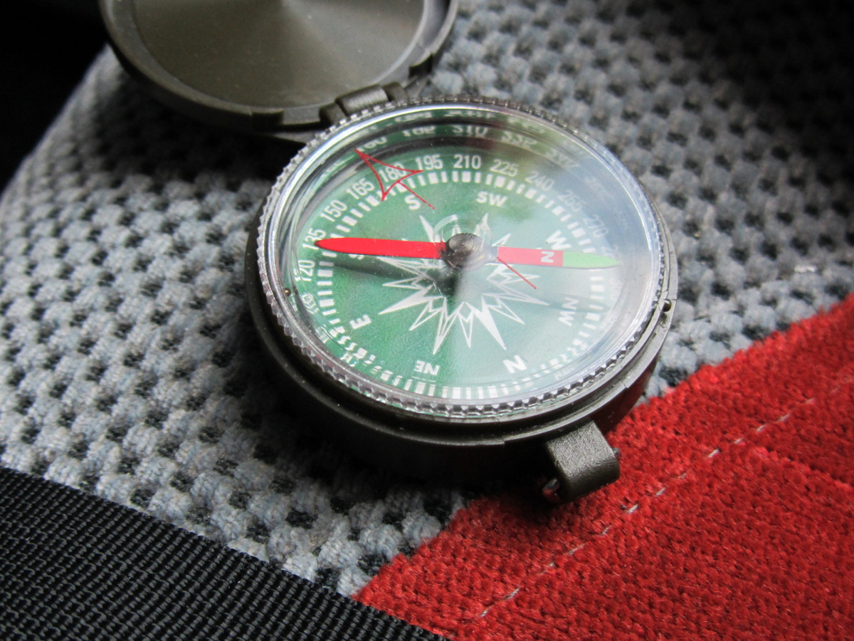 A compass with a green face sits open on a fabric background