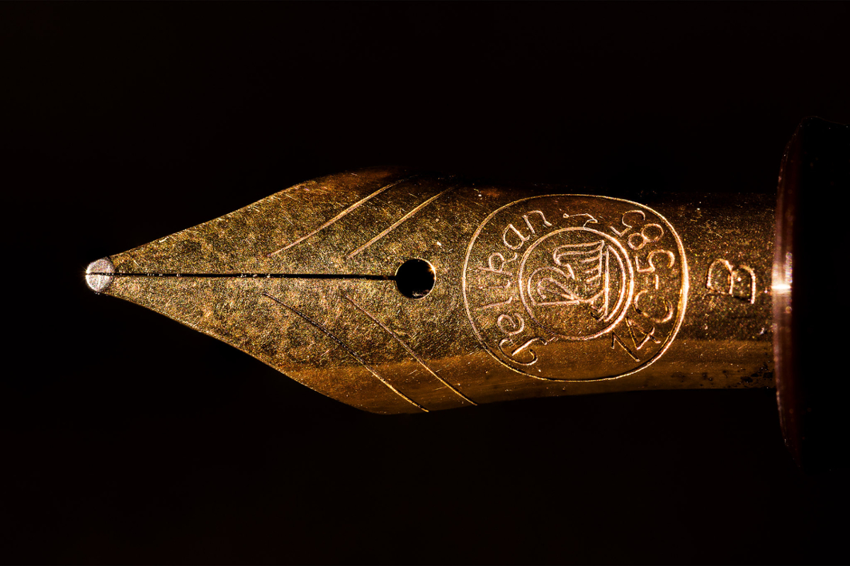 A close up of a gold fountain pen tip on a black background
