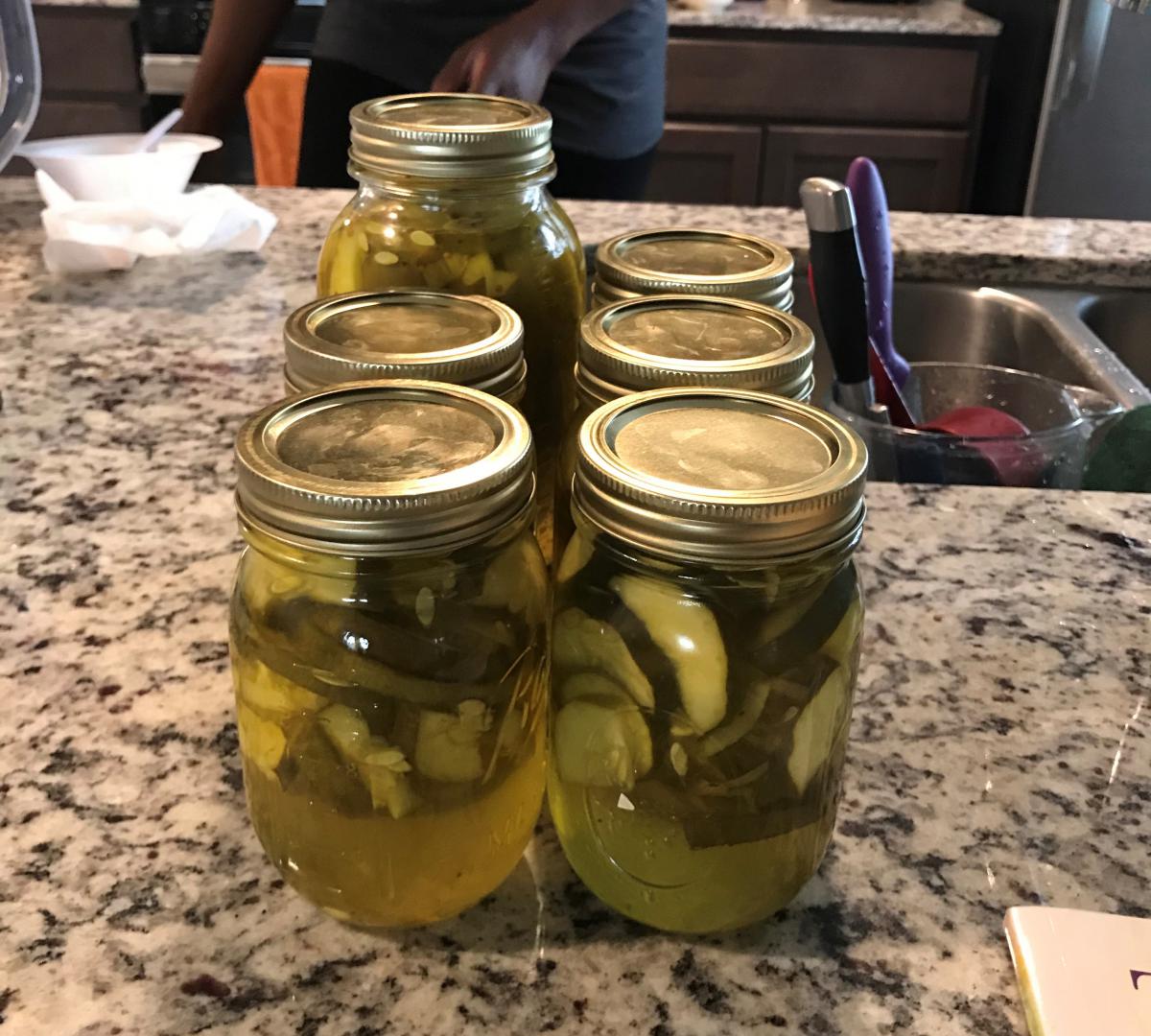 Six mason jars filled with homemade pickles on a granite countertop.