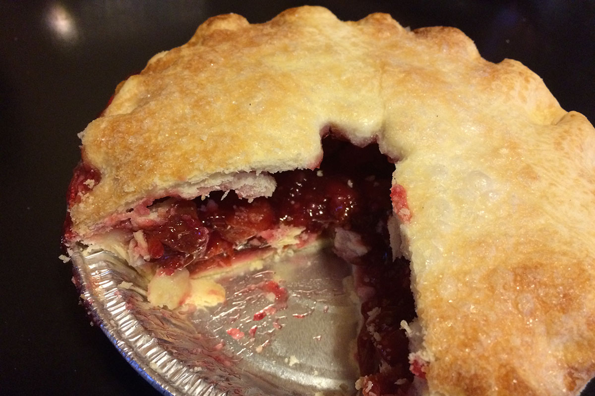 Small, double crust cherry pie in a foil pan, with a piece taken out.