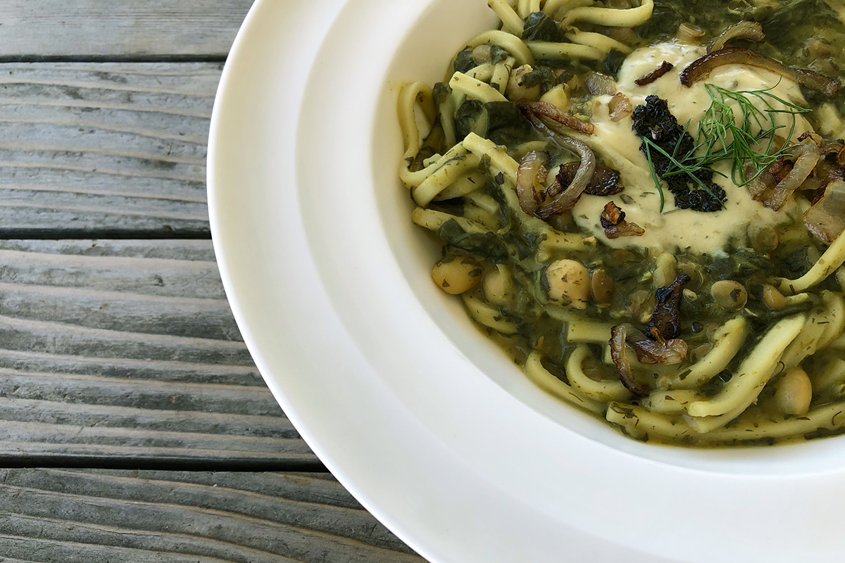 A white bowl with noodles and a greenish sauce and chickpeas