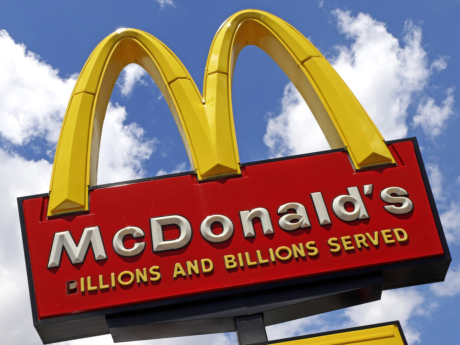 photo of McDonald's logo at an angle, blue sky with small white clouds in the background