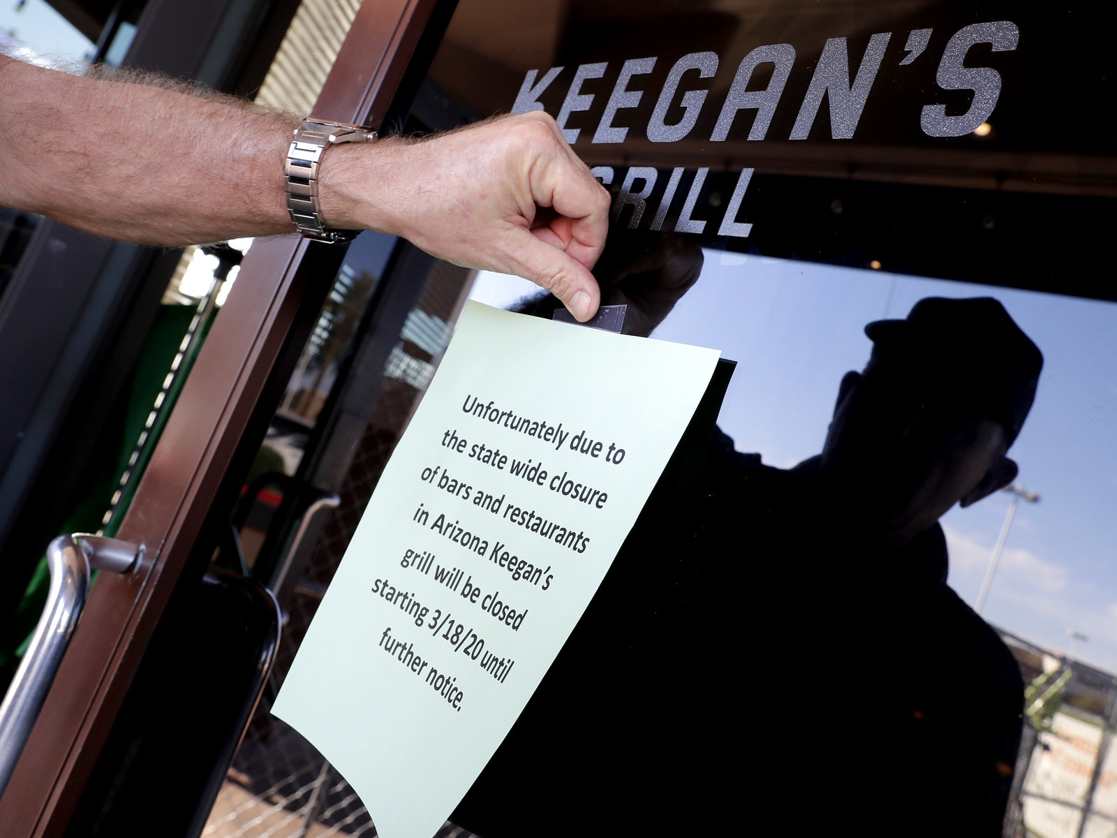 A hand taping a notice to a glass door, announcing the closure of a restaurant in Arizona.