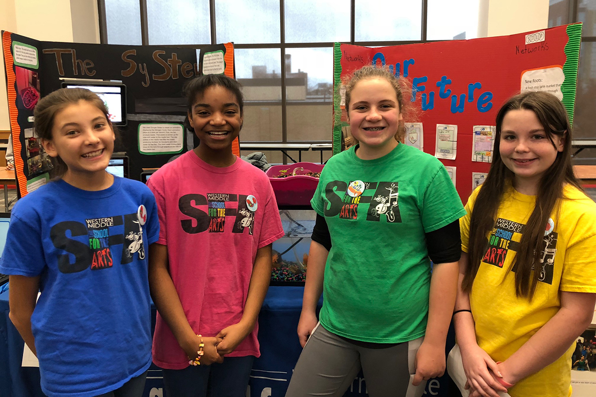 Four middle school-aged girls standing in front of a science fair display