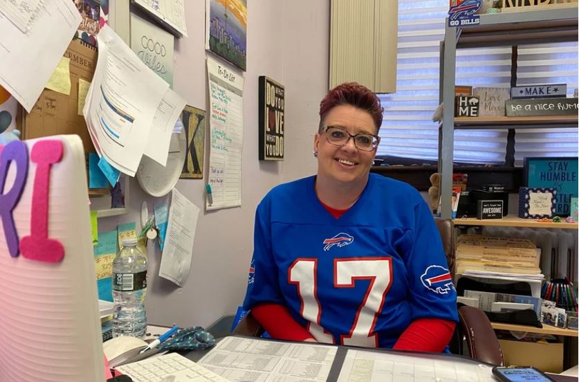 a woman in a footbal jersey at a desk smiling at camera