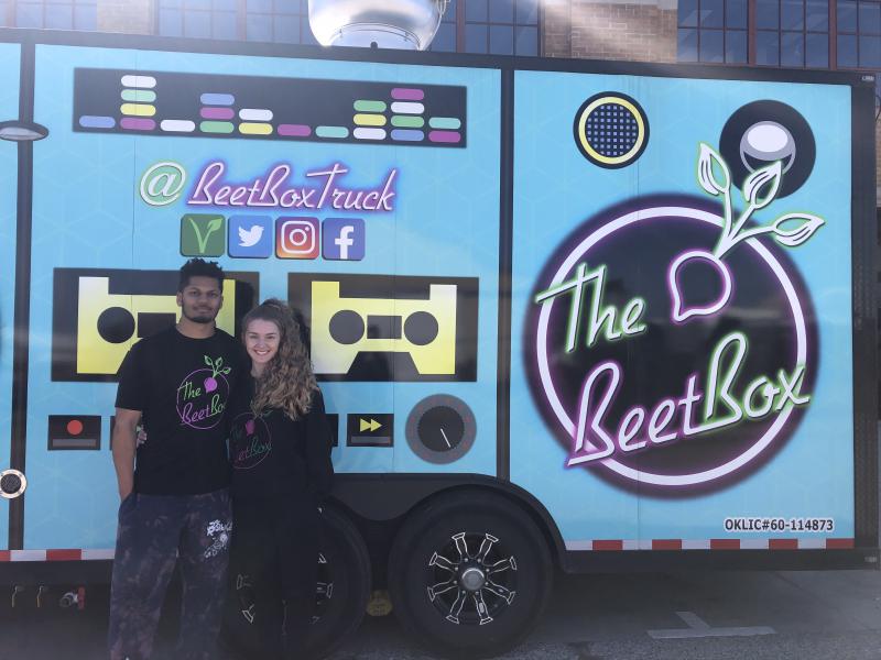 Two young people standing in front of a painted graphic of a portable cassette player, with a "Beet Box" logo in a circle.