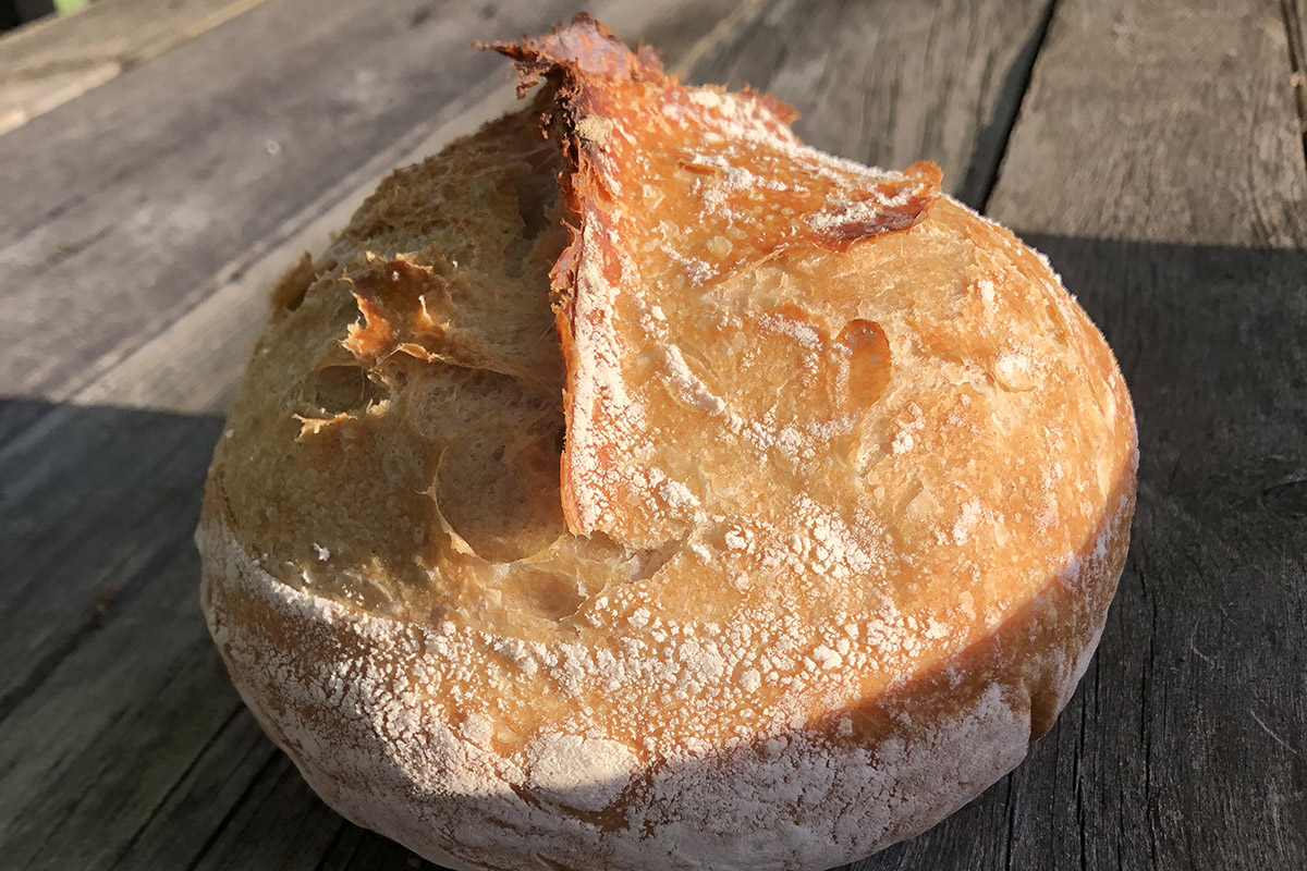 Round loaf of artisan-style bread on a wooden table in the sunlight