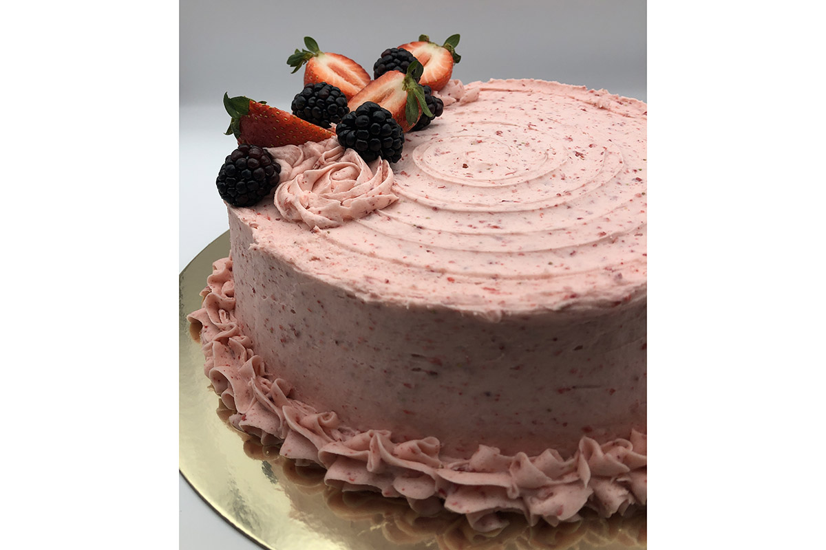 round cake frosted with pink speckled icing, decorative icing roses and border along the bottom edge on a shiny gold cake board