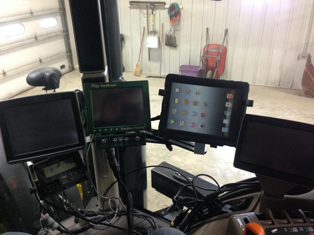 Three electronic screens, a dashboard for a tractor, inside a metal-sided barn.