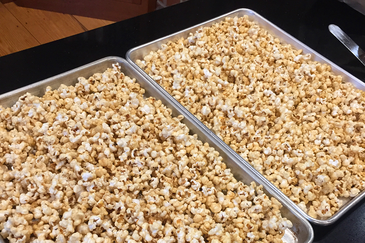 Two half-sheet metal baking pans filled with a single layer of caramel popcorn