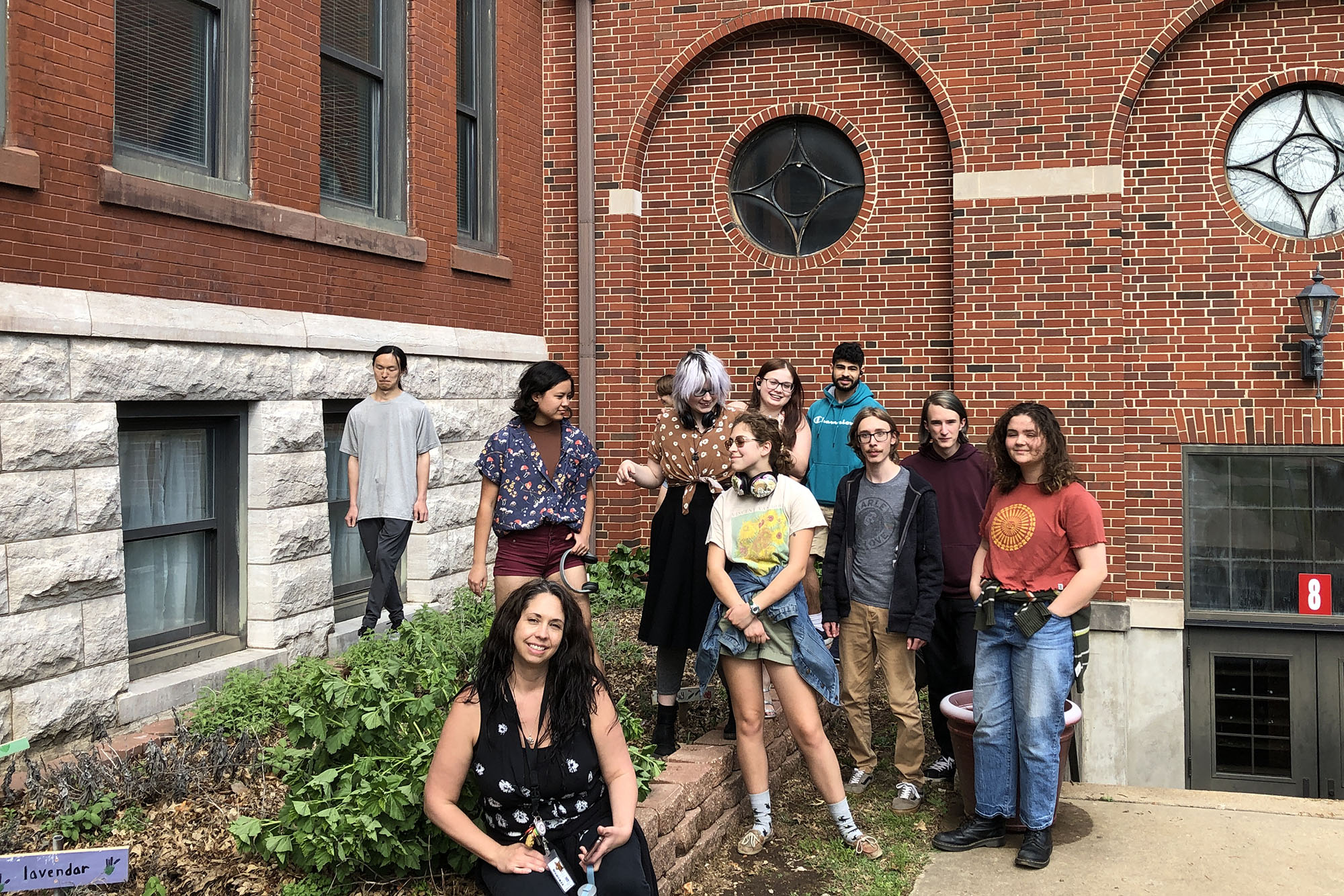a candid shot of a group of 11 people around a garden bed against a backdrop of an historic brick and stone building.