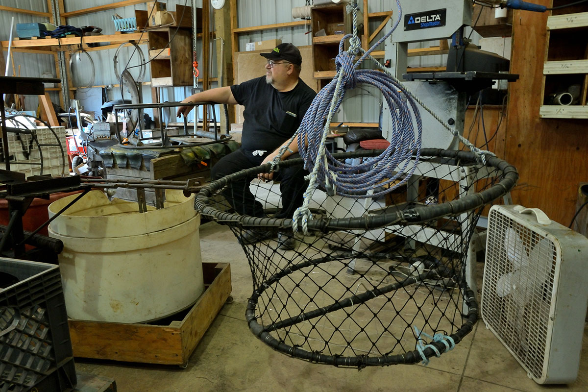 Leonard Van Curler sits in a crowded workshop with a crab net in the foreground.