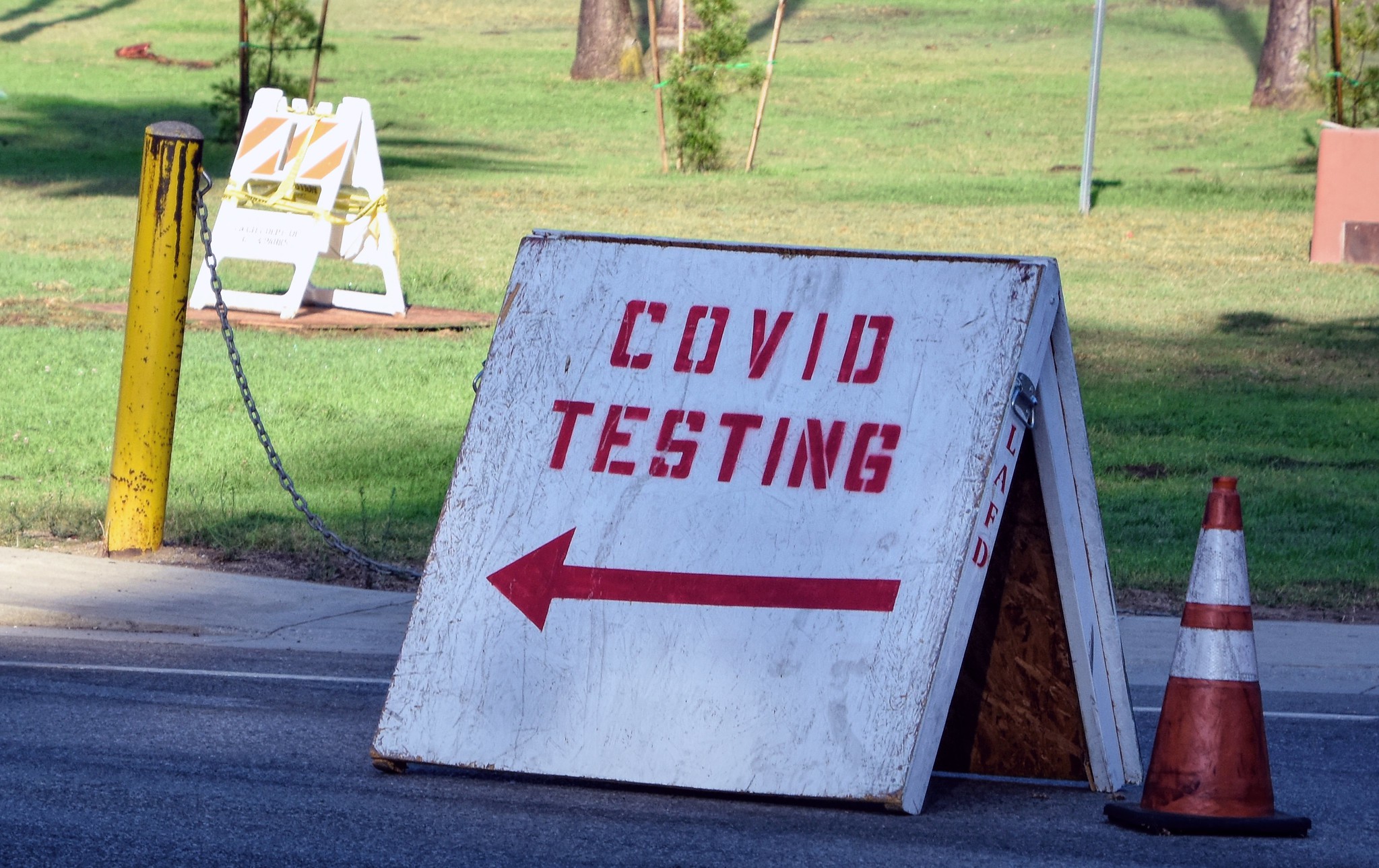 A painted wooden, sandwich-board style sign saying "covid testing" with an arrow pointing left in a parking lot. 
