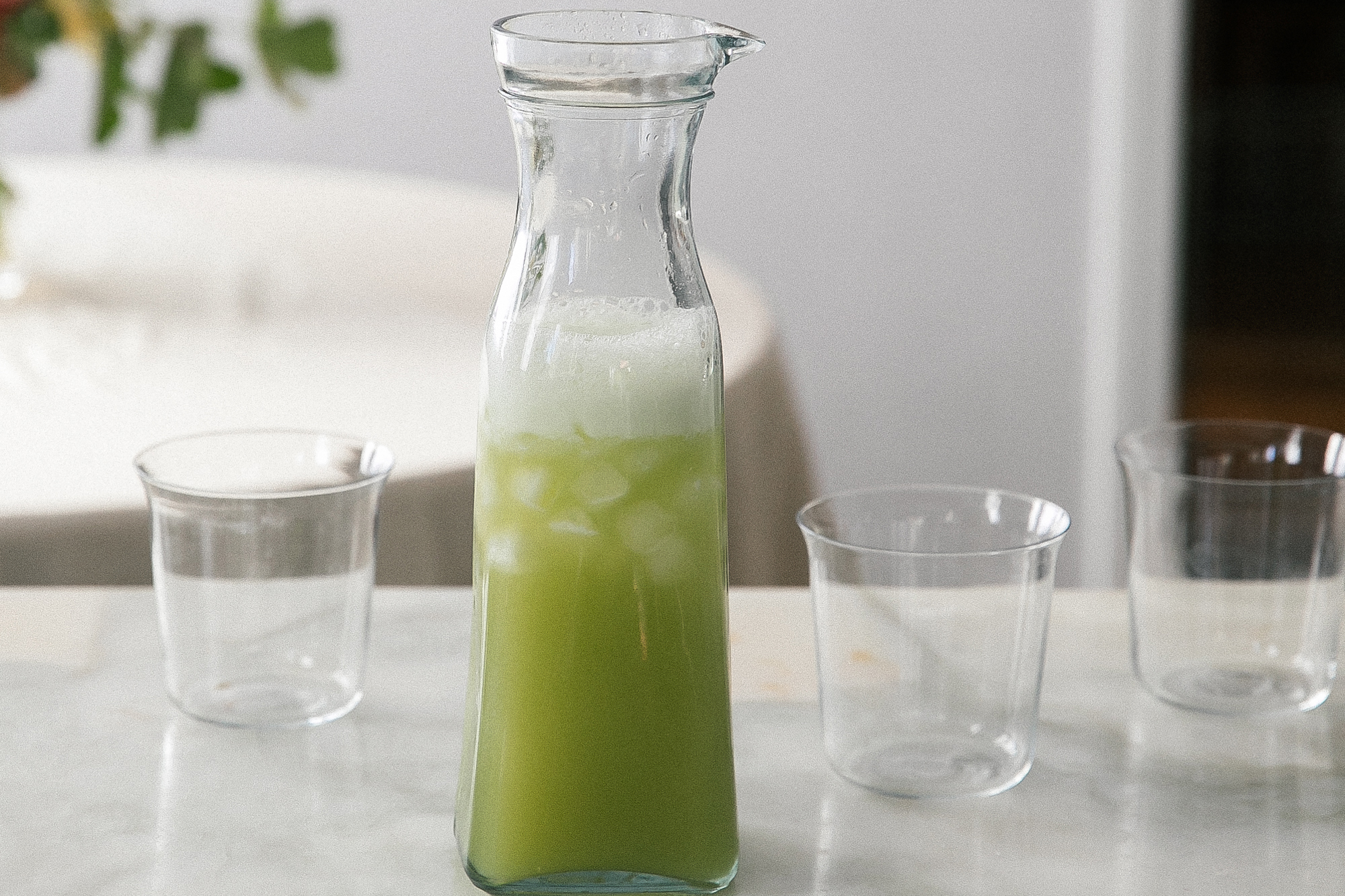 Glass carafe with cucumber juice plus three glasses.