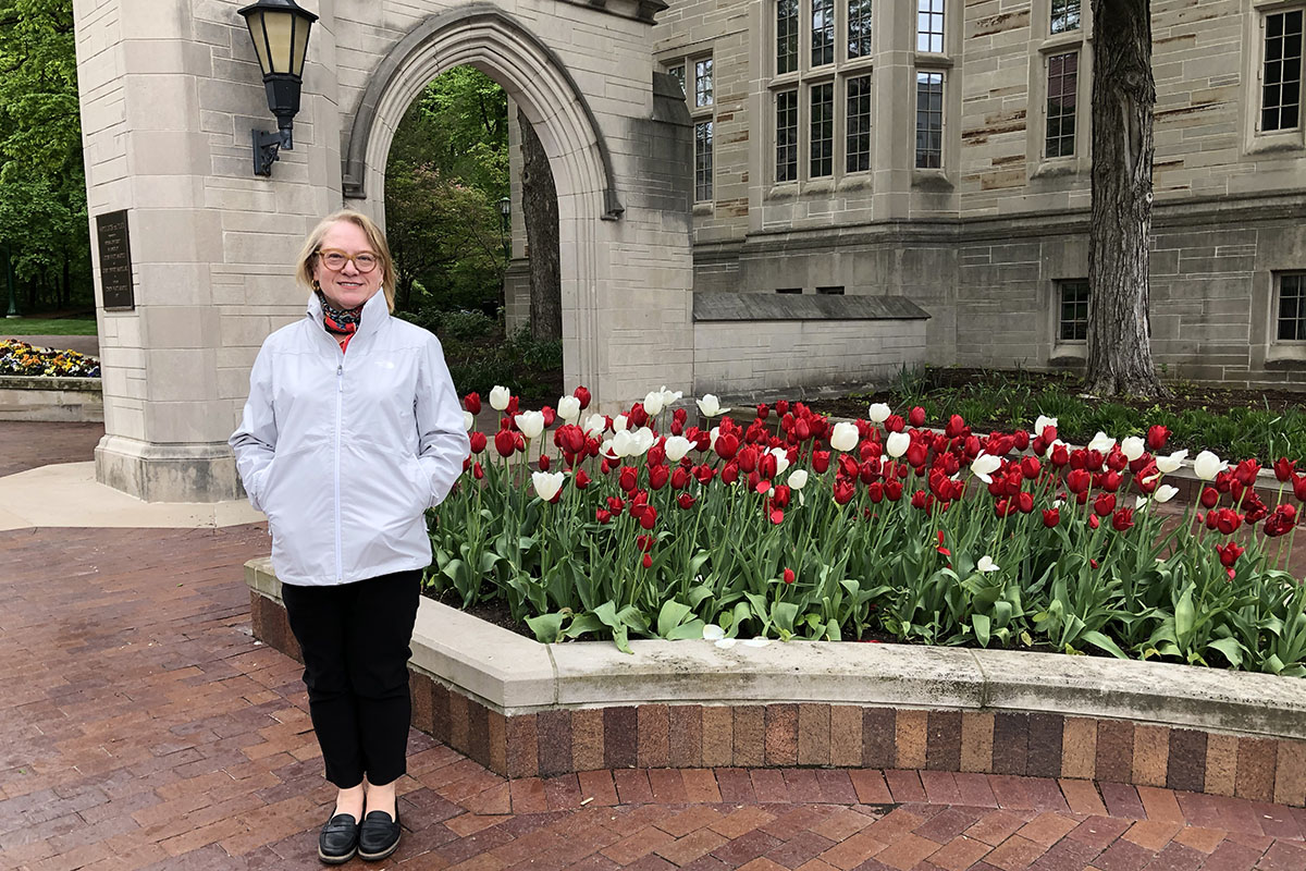 Elizabeth Dunn standing in front of a bed of red and white tulips near the a limestone arched wall.