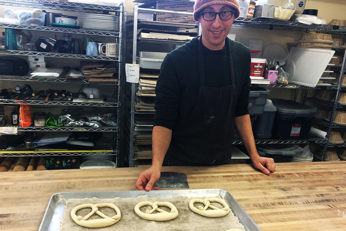 Baker, Eric Schedler with sheet pan of unbaked pretzels, in his bakery