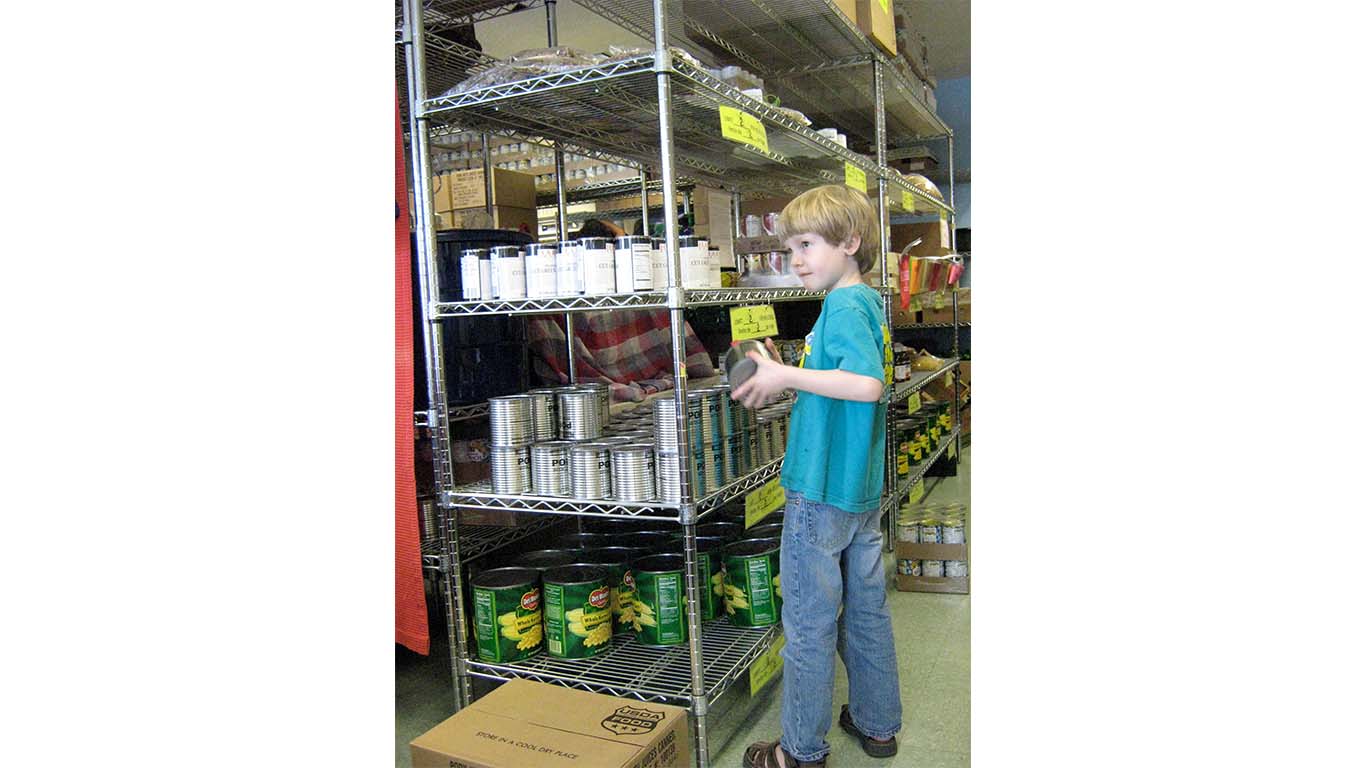 small child stocking a shelf in a food pantry with canned goods