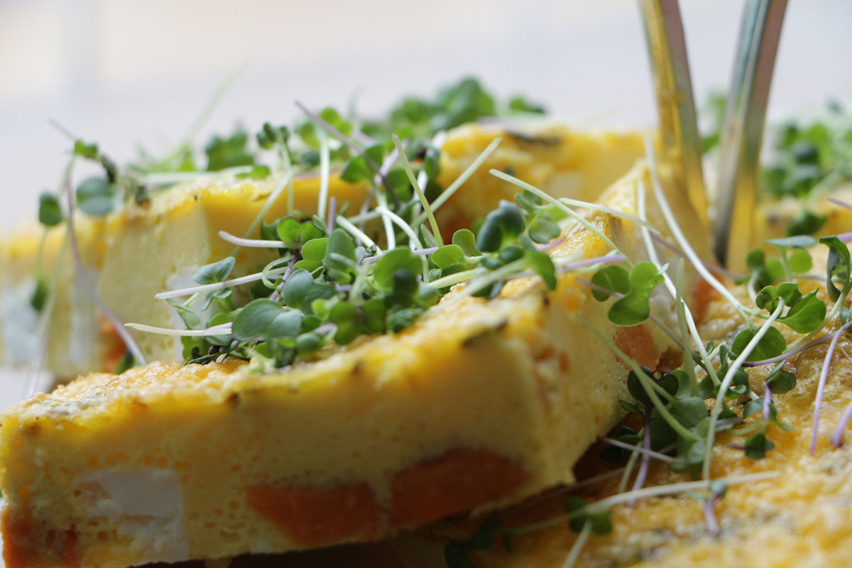 Close up of a some slices of frittata with feta and sweet potato and green sprouts sprinkled on top