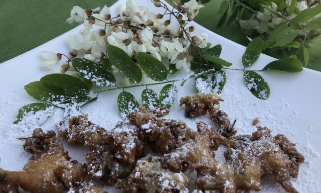 fried food with white sugar sprinkled on top, on a white square plate on a green tablecloth, with white flowers arranged around the plate