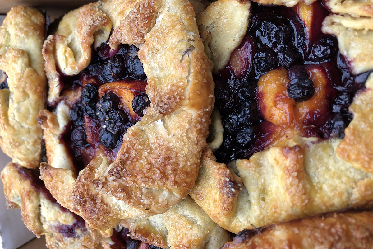 Rustic fruit tarts filled with peaches and blueberries arranged in  box.