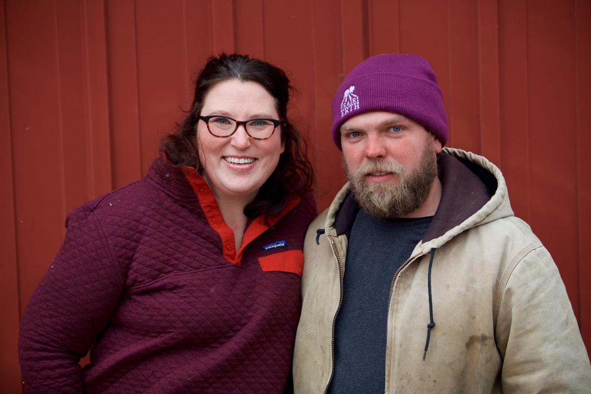 Hans and Katie Bishop, in winter wear, head and shoulders view against a red wood siding background