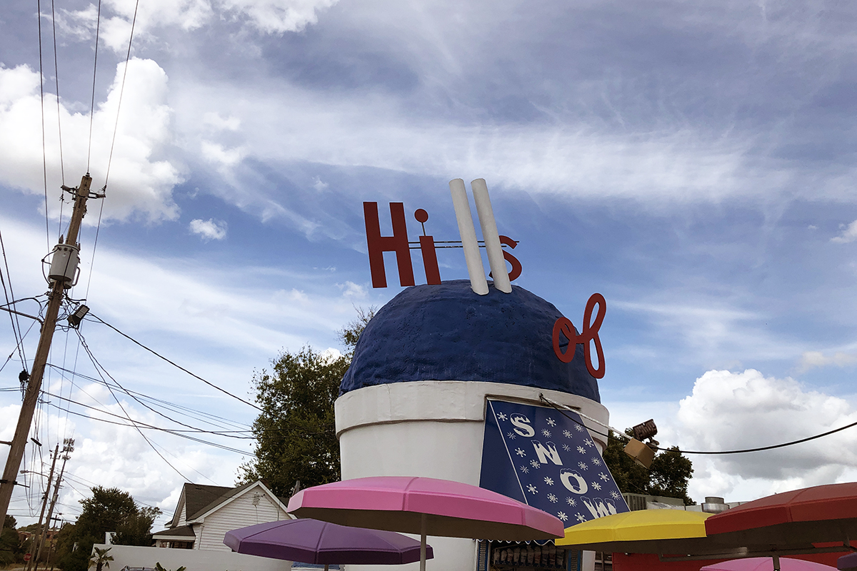 A snow cone stand shaped like a snow cone, with colorful umbrellas in front. 