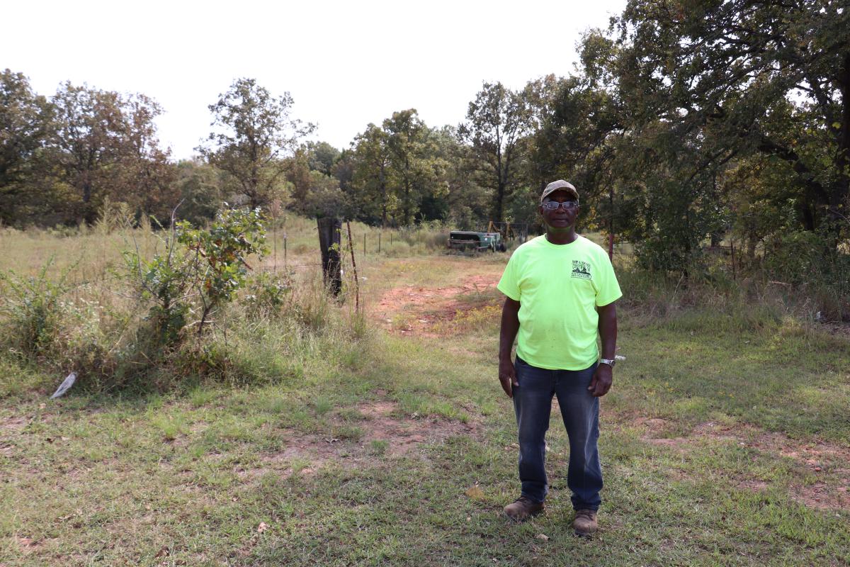 Nathan Bradford stands in a partially wooded area near a fence.