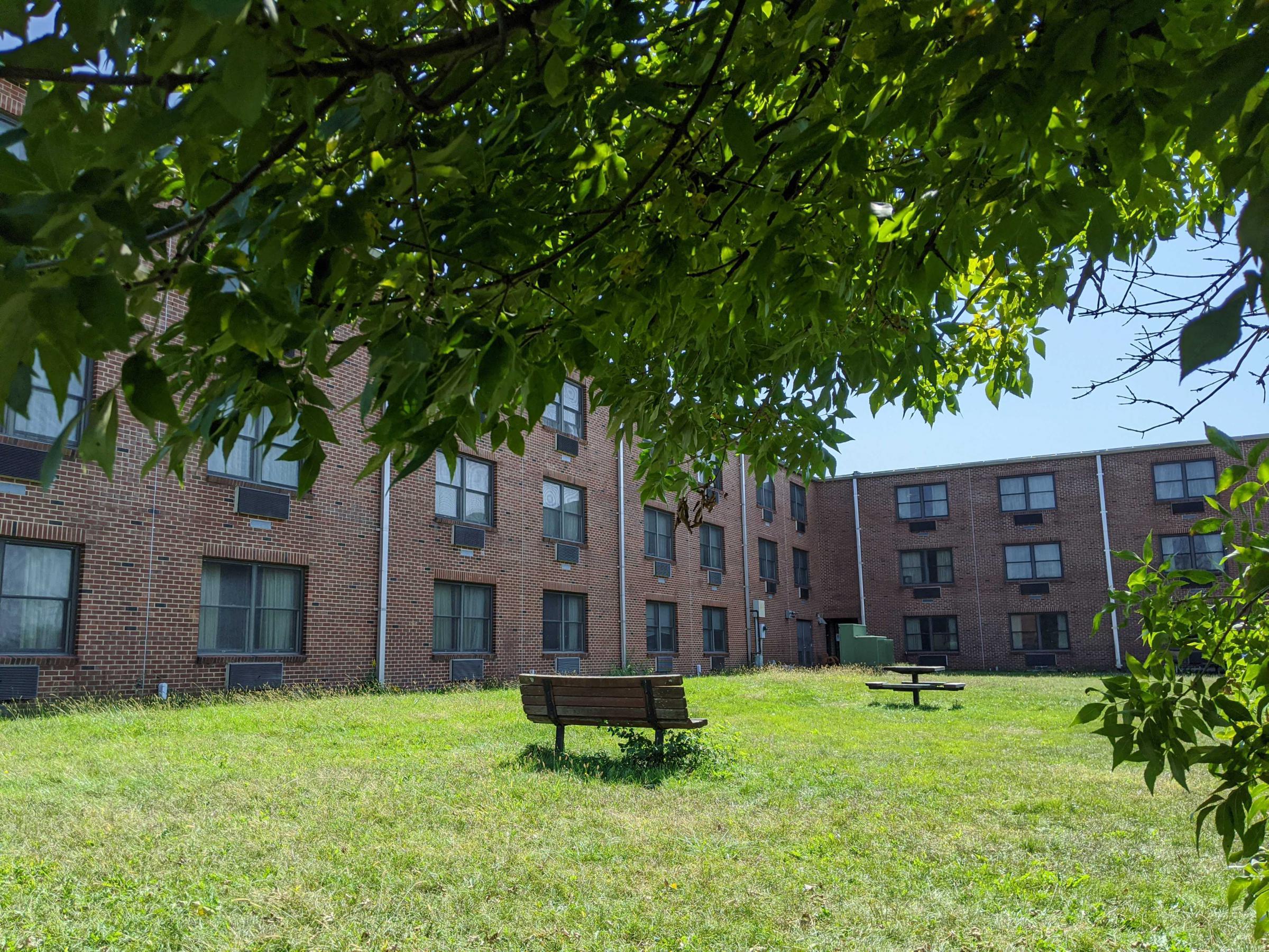 A grassy area surrounded by a two story brick building with uniform windows and air conditioners.
