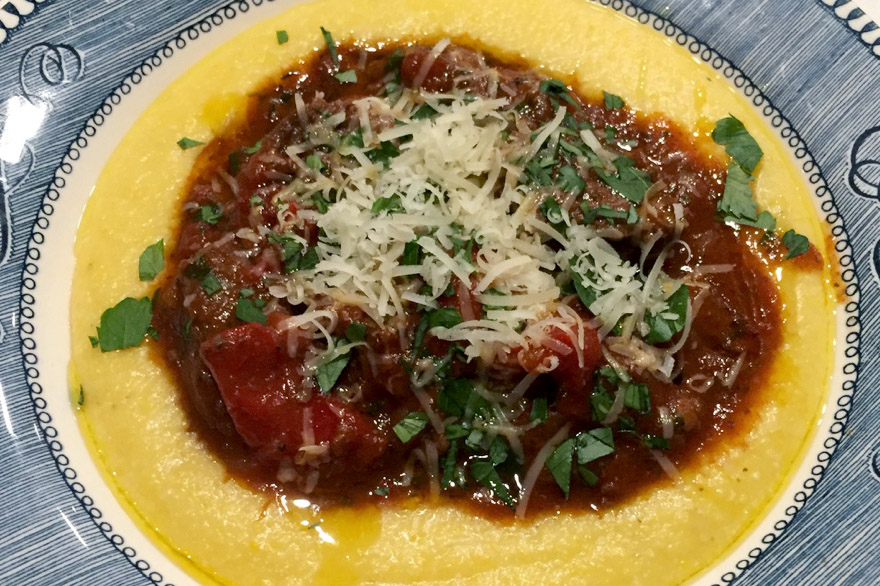 Chunky red sauce on a bed of golden polenta with parsely and grated cheese garnish.