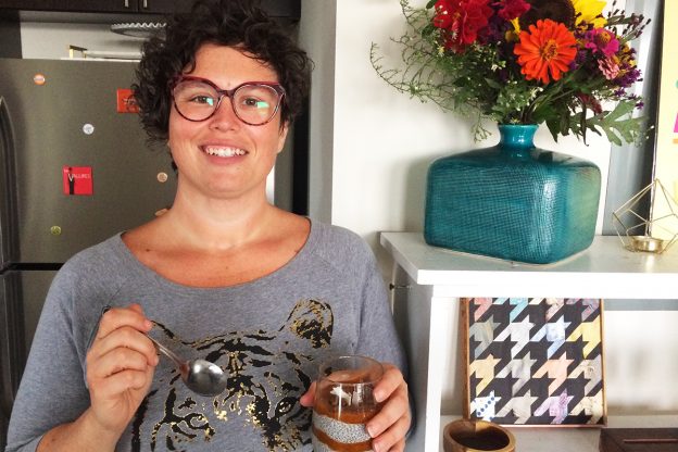 Jackie Bea standing in her kitchen with a glass filled with a chia pudding parfait.