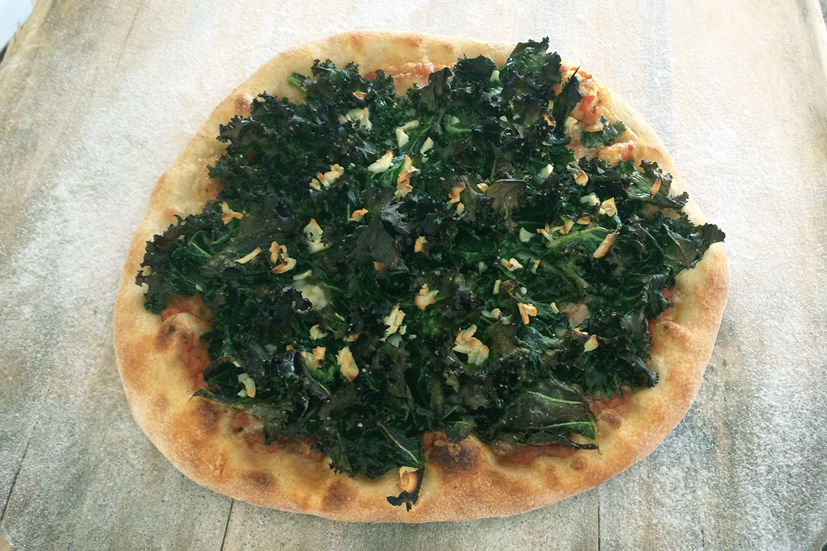 A small pizza piled with dark green kale